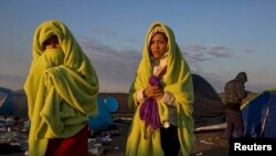 Hungary -- Migrants wrap themselves in blankets to warm up as the sun rises at a collection point in the village of Roszke, September 9, 2015